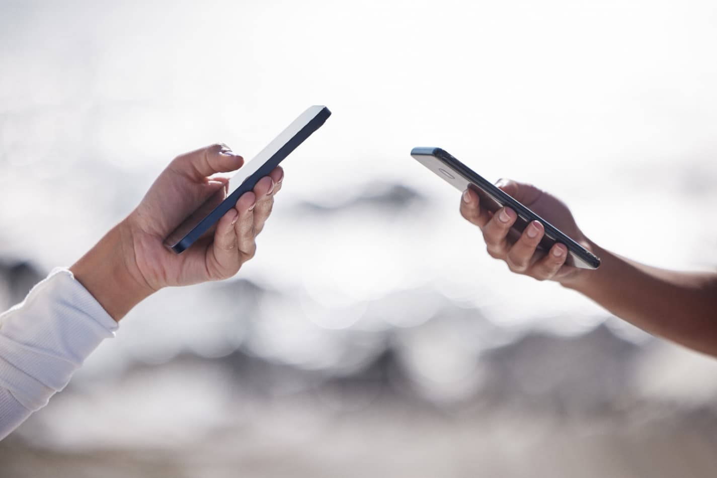 Two hands holding their smartphones toward each other to exchange details
